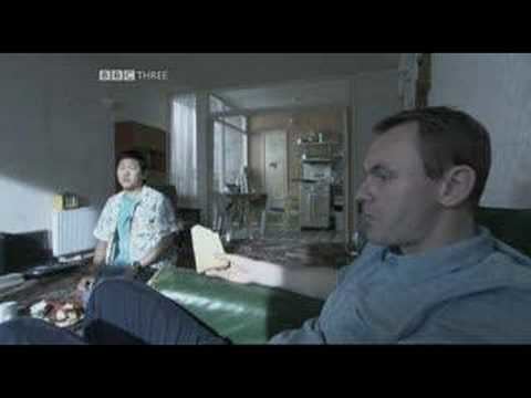 Sean Lock and Benedict Wong sitting on the couch in a scene from the 2002 sitcom 15 Storeys High