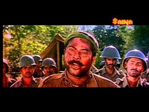 Mammootty as Khadir with a mustache, wearing a green headband, and brown shirt with soldiers at his back wearing army hats in a movie scene from 1921, a 1988 Indian historical war film.