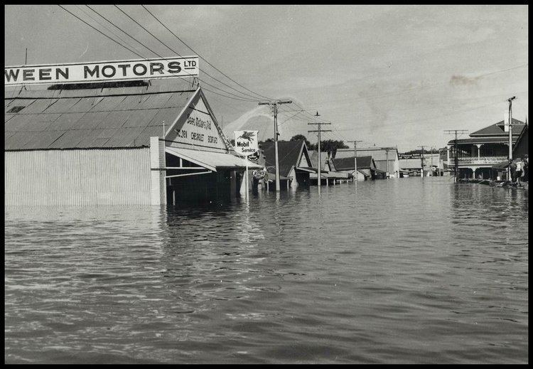 1956 Murray River flood, has flooded street with houses and electric post from left to right.