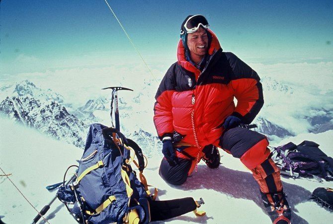 A man climbing the K2 Mountain while wearing a black and red jacket