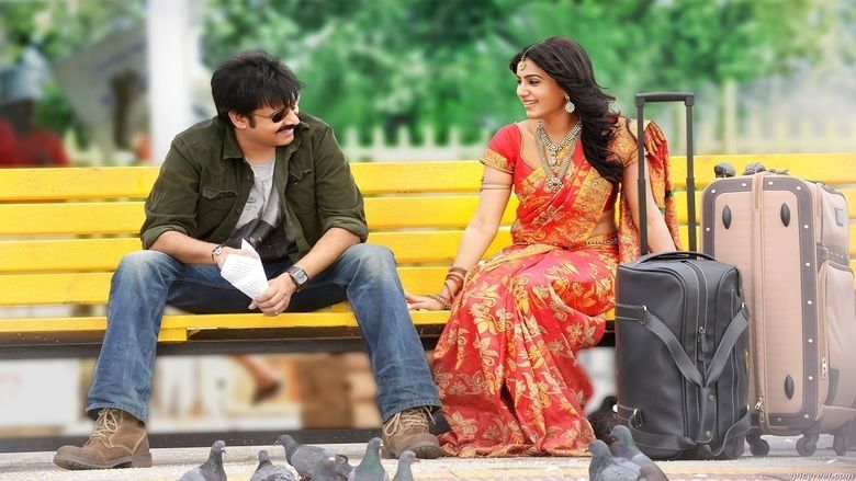 Pawan Kalyan and Samantha Ruth Prabhu smiling and looking at each other while sitting on a bench. Pawan wearing sunglasses, a green jacket over a gray shirt, and blue pants while Samantha with long hair, and wearing red and yellow sarees in a movie scene from Attarintiki Daredi (2013 film).