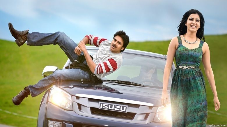 Pawan Kalyan lying in the car while Samantha Ruth Prabhu is smiling. Pawan wearing a red and gray long sleeve shirt and blue pants while Samantha wearing a necklace and a green sleeveless dress in a movie scene from Attarintiki Daredi (2013 film).
