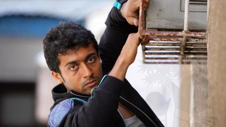 Scene from Ayan featuring Suriya as Devaraj Velusamy with a serious face and wearing a jacket.