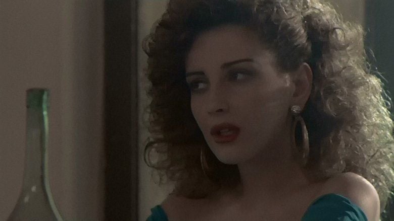 Francesca Dellera as Rosalba looking at something and wearing large golden earrings and a green off shoulder dress in a scene from Capriccio,1987.