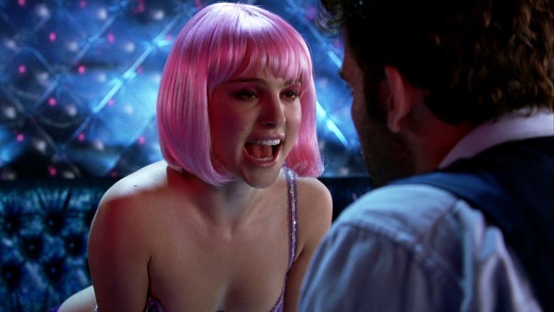 In the movie scene of Closer 2004,in a strip bar room with a black wall, Natalie Portman is serious, leaning forward, mouth open, has pink hair wearing lingerie, in front is Clive Owen looking at her, has black hair shaved beard, wearing a white polo under a black vest.