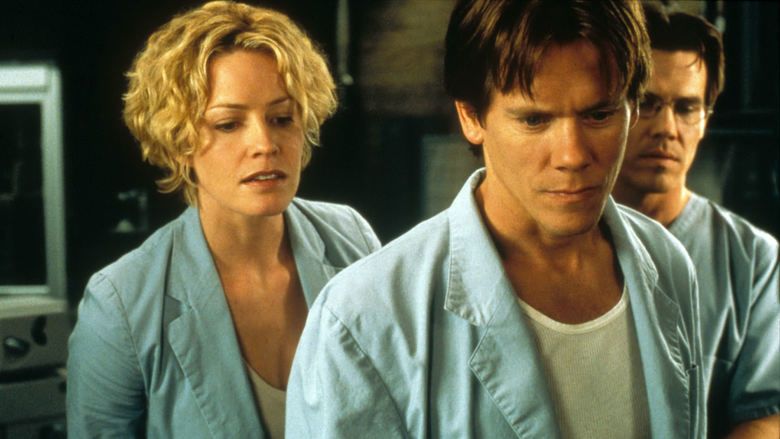 Elisabeth Shue, Kevin Bacon, and Josh Brolin (from left to right) with serious faces while looking at something and all of them are wearing blue scrub suits in a movie scene from Hollow Man, a 2000 science fiction thriller film.