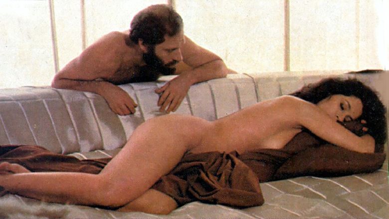 Sônia Braga as Maria sleeping and lying on a sofa while Paulo César Peréio as Paulo watching her. Sônia is naked and covered with a piece of brown cloth while Paulo is also naked, with a beard and mustache in a movie scene from I Love You (1981 film).