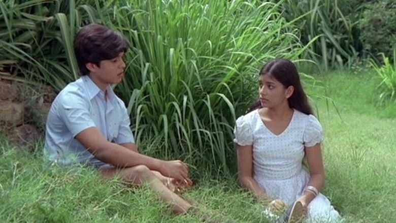 Master Raghu and Devi are talking to each other while sitting on the grass with serious faces. Master Raghu is wearing a blue polo shirt while Devi is wearing a white dress and bracelet