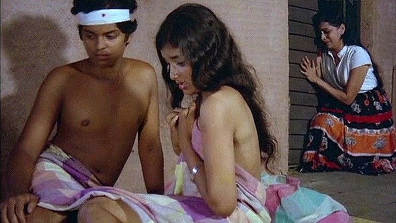 Master Raghu and Devi (left) looking at something while covering their naked body with a purple and blue blanket. Master Raghu with a bandage on his head and Devi with a worried face. A woman (right) crying beside the door while wearing a white blouse and black and orange long skirt in a scene from the 1982 Malayalam film, Ina