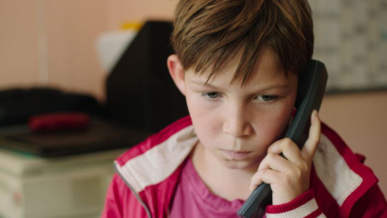 The movie scene of Jack (2014 film),  in the middle of a room, Ivo Pietzcker is serious, standing, talking to the phone in his left ear holding with his left hand, has brown hair, wearing red shirt under a red jacket