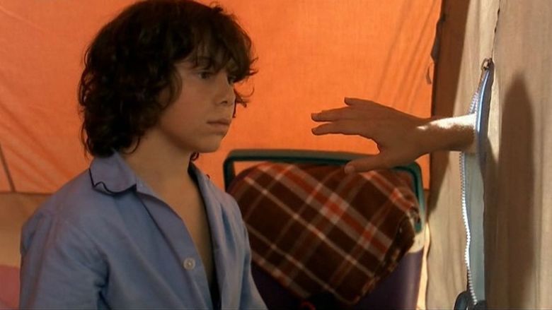 Marc Beffa with a serious face while looking at a hand, with curly hair from a movie scene of La Fonte des Neiges, a 2009 short comedy-drama film. He is wearing blue long sleeves.