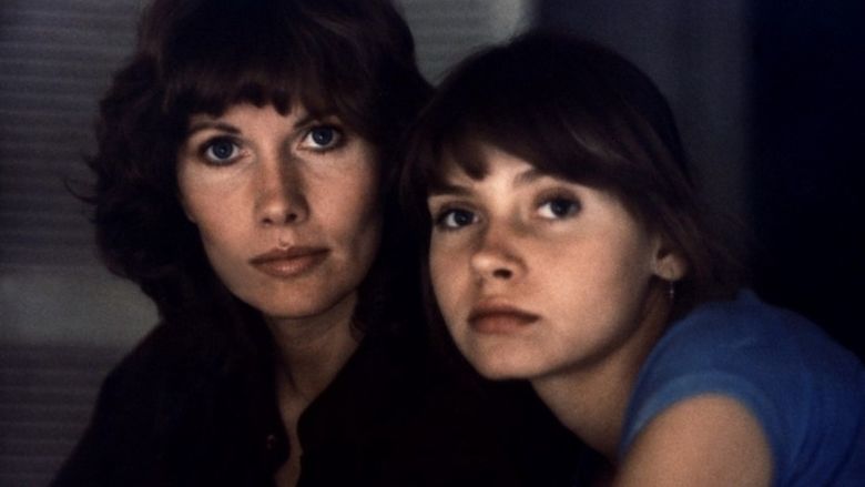 In the Laura (1979 film) movie scenes, Sarah (left) is serious, has black hair, wearing a black top. Laura (right) is serious, has black hair, wearing silver earrings and a blue top.