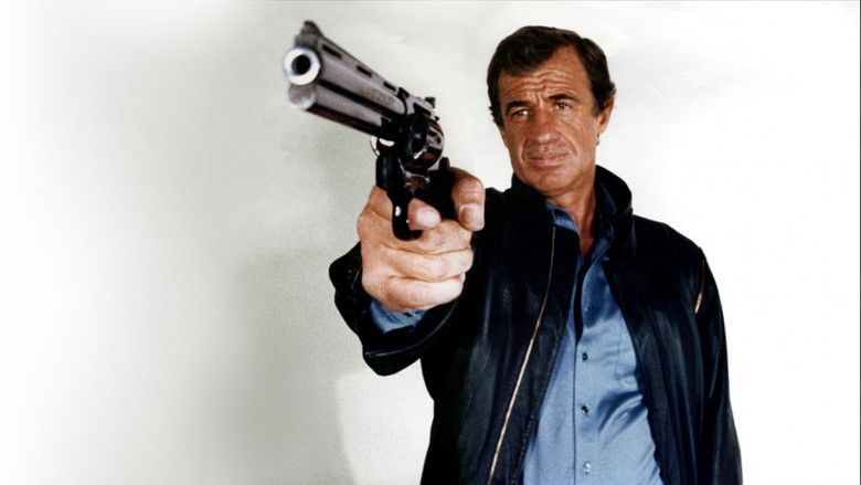 Jean-Paul Belmondo as Josselin Beaumont dit 'Joss' with a serious face while holding a gun and wearing a black jacket over a blue polo shirt in a movie scene from Le Professionnel, a 1981 French action thriller film.