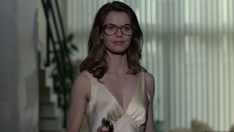 Cyrielle Clair as Alice Ancelin smiling, with wavy hair, wearing eyeglasses and a light gold sleeveless dress in a movie scene from Le Professionnel, a 1981 French action thriller film.