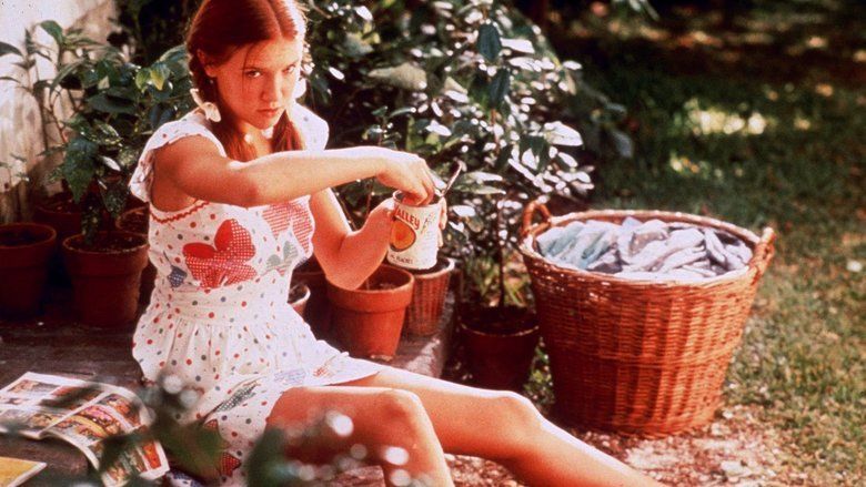 Dominique Swain as Lolita holding a cup and wearing a white, floral designed dress in a scene from Lolita, 1997.