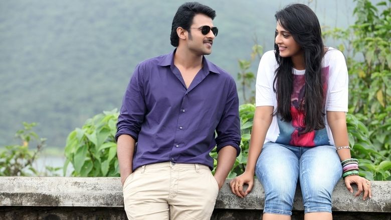 Prabhas and Anushka Shetty smiling while staring at each other and sitting on a fence in a scene from the 2013 action drama film, Mirchi