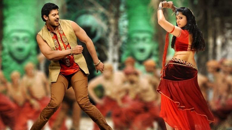 Prabhas dancing and wearing a beige vest, red polo, and brown pants while Anushka Shetty wearing a red dress in a scene from the 2013 film, Mirchi