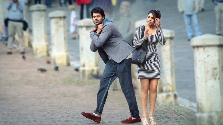 Prabhas dancing and wearing a gray coat and pants while Richa Langella looking at him in a scene from the 2013 action drama film, Mirchi