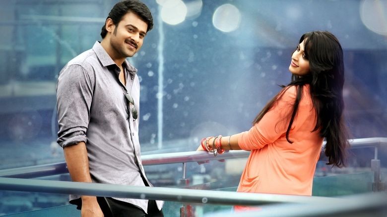 Prabhas smiling while wearing a gray long sleeve and Anushka Shetty wearing an orange long sleeve blouse in a scene from the 2013 film, Mirchi