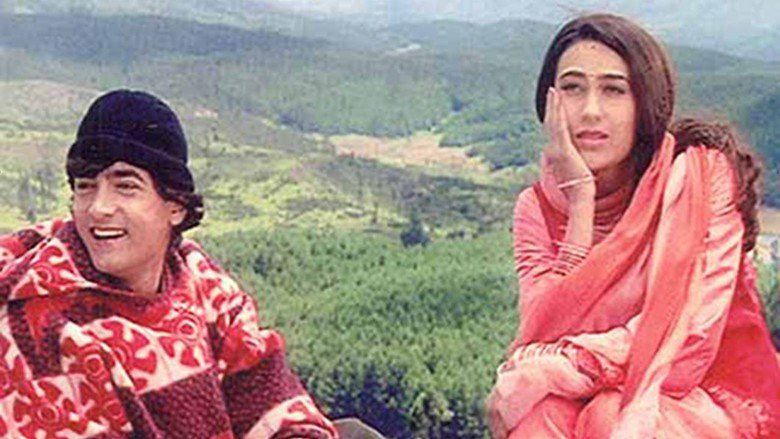 The movie scene from "Raja Hindustani" (1996) featuring Aamir Khan as Raja Hindustani, and Karisma Kapoor as Aarti Sehgal sitting together on top of the mountain