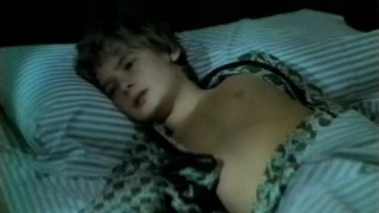Mark Lester lying on the bed while wearing black and gray sleepwear in a scene from the 1971 horror film, What the Peeper Saw