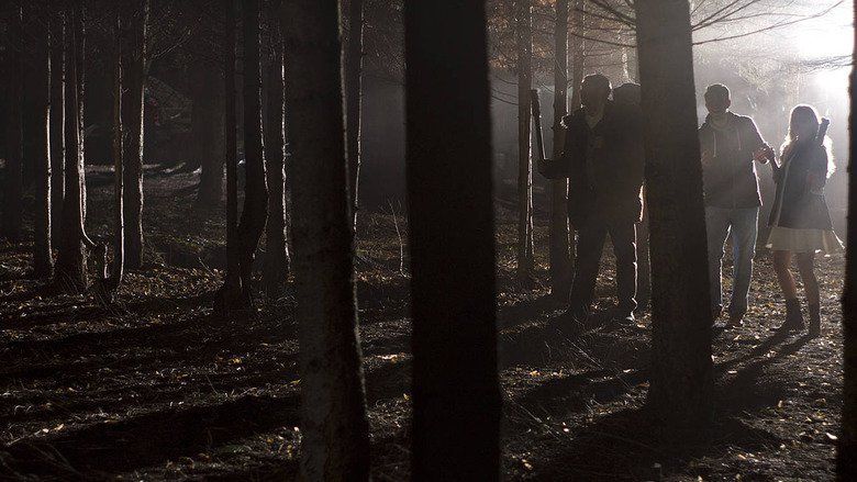 In the movie scene of Wrong turn 6 last Resort 2014, .three people wandering in the forest, from left  Sadie Katz (right) is standing while holding a baseball bat wearing white shirt, pants and a jacket, in the middle is Anthony Ilott standing holding the hand of the Sadie Katz (right) wearing  hoodie jacket, denim pants, and from the right Sadie Katz is standing holding hand with Anthony Ilott beside her has long hair wearing white dress and a jacket.