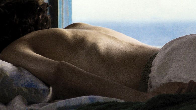 Ines Efron as Alex Kraken having a short curly hair, lying on the bed in a back position with a brown curtain and window in the background, topless, and wearing white shorts