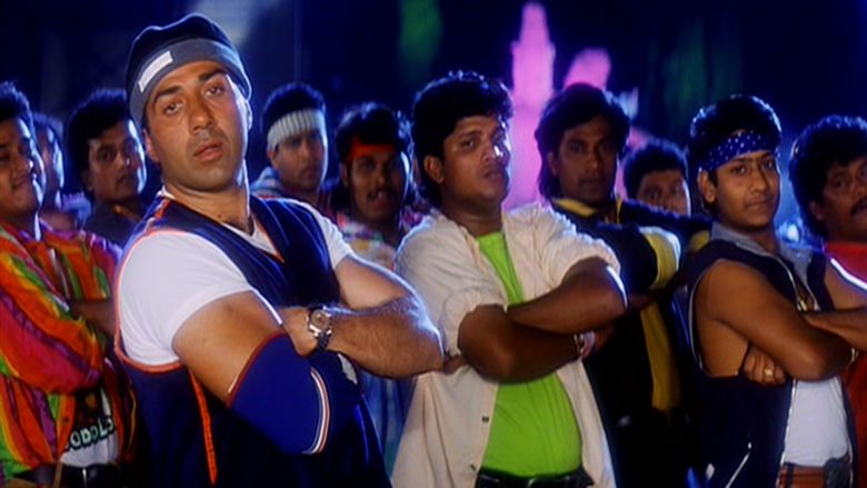 A scene from Ziddi, a 1997 Indian action film featuring Sunny Deol as Deva Pradha wearing a hat, blue jersey, white shirt, and a watch with 10 people on his back.