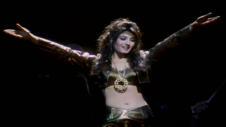 A scene from Ziddi, a 1997 Indian action film featuring a woman wearing a jacket, a big necklace, and a sexy top and skirt.