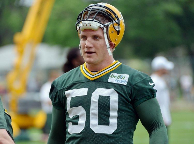 A J Hawk talking and looking to someone, he has blonde hair wearing a yellow helmet, green long arm sleeves, and a green jersey with a #50 on it and a sponsored name “bellin heath” on the left side