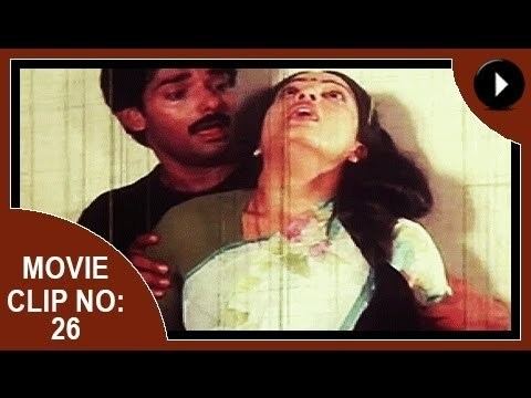 Movie clip no. 26 of Aadhi Thaalam, a 1990 Indian Malayalam film starring Jayarekha with a stunned face while leaning on a man with a mustache, with long hair, and wearing a white and green Indian dress.