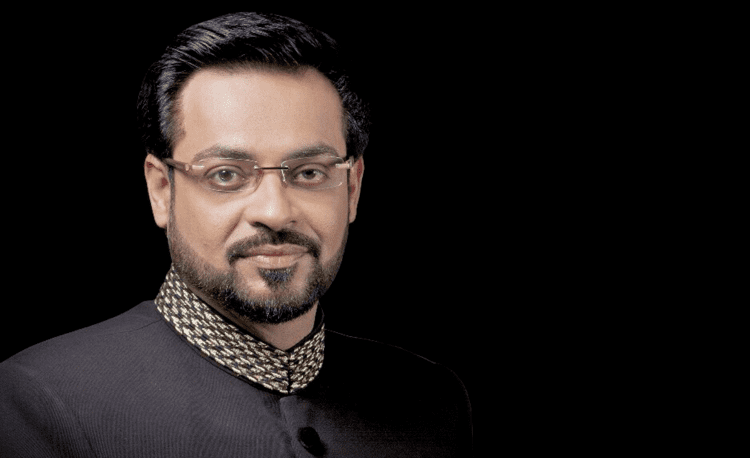 Aamir Liaquat is serious, has black hair, a beard, and a mustache, wearing eyeglasses, and black shalwar kameez.