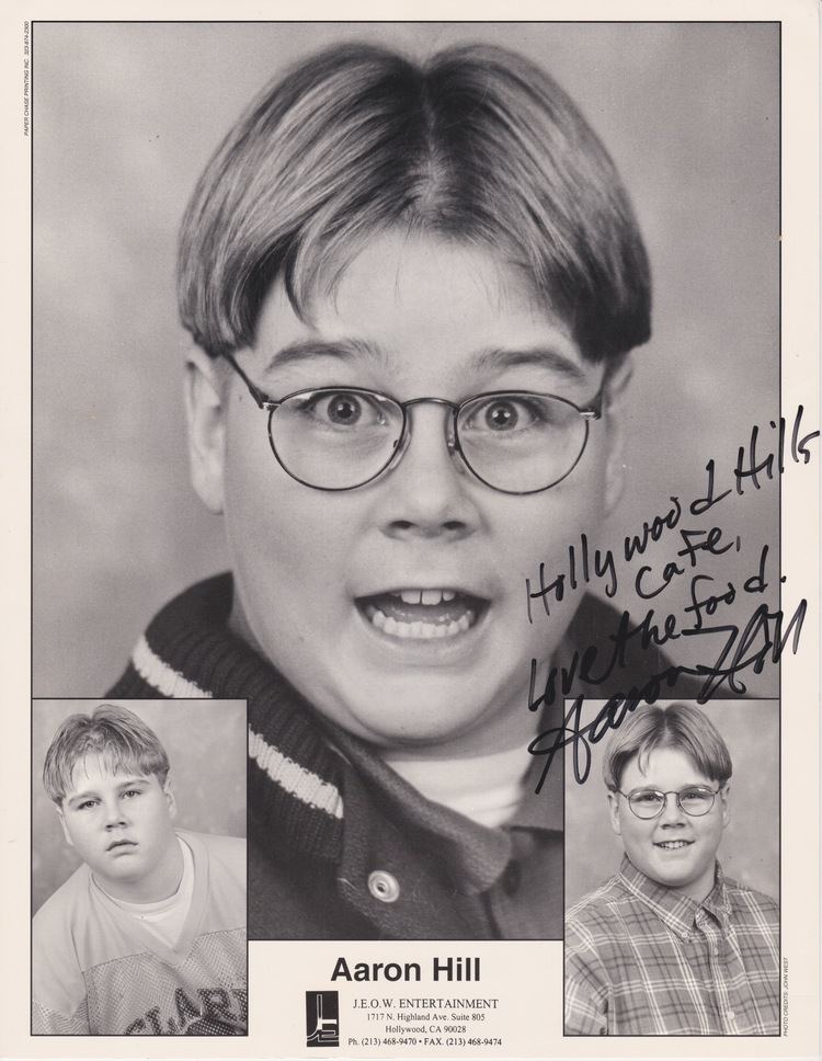 Poster of Aaron Hill with autograph, wearing eyeglasses and showing his teeth. On the left lower part, Aaron Hill with a serious face, and on the right lower part, Aaron Hill with a smiling face, wearing eyeglasses, and a checkered polo shirt.