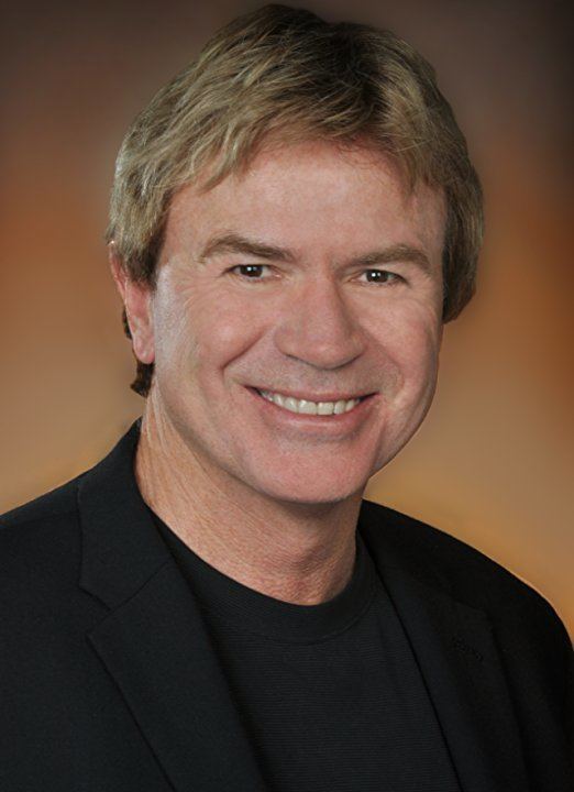 Aaron Norris smiling in a black shirt and suit