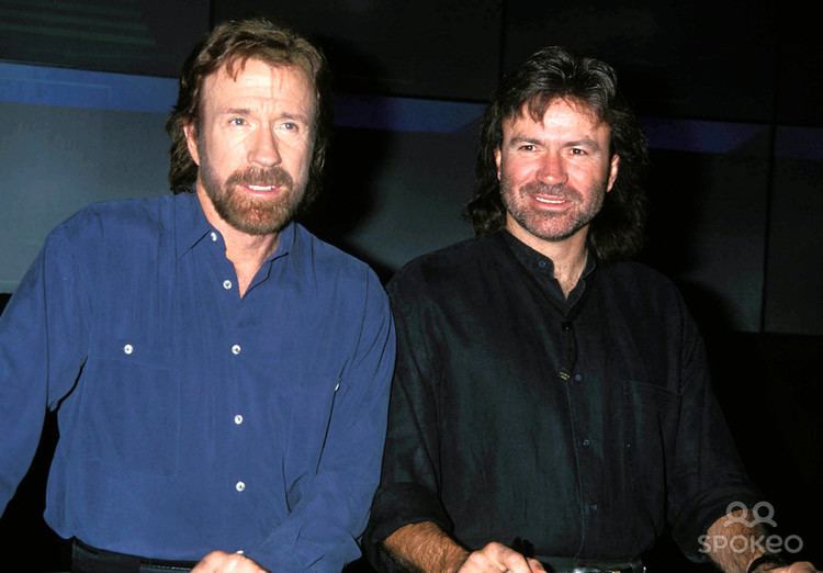 Chuck Norris smiling in blue sleeves with his younger brother Aaron Norris in black sleeves
