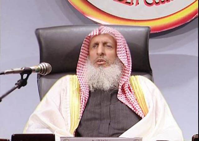 Abd al-Aziz ibn Baz speaking in a meeting with a thick white beard and wearing a red and white kufiyah.