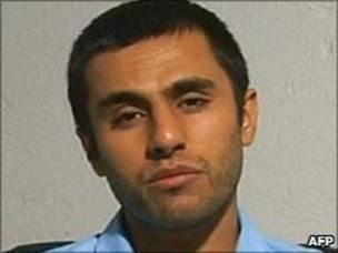 A mugshot of Abdolmalek Rigi during his imprisonment with facial hair and wearing a blue shirt.