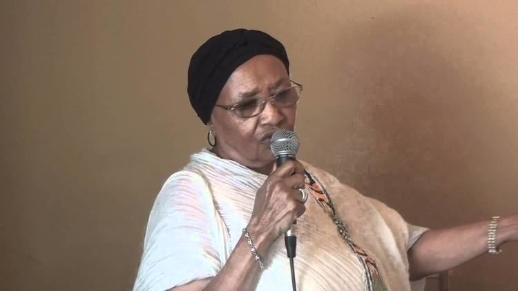Abebech Gobena talking and holding a microphone while wearing a white sleeve and eyeglasses
