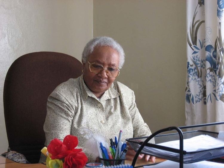 Abebech Gobena sitting on a chair while wearing a long sleeve and eyeglasses