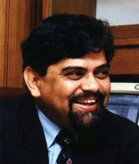 Achyut Godbole wearing black coat and blue long sleeves while smiling