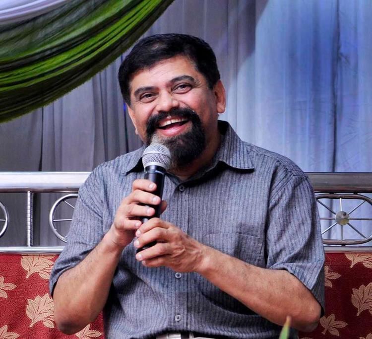 Achyut Godbole wearing blue and gray polo while holding a microphone and smiling