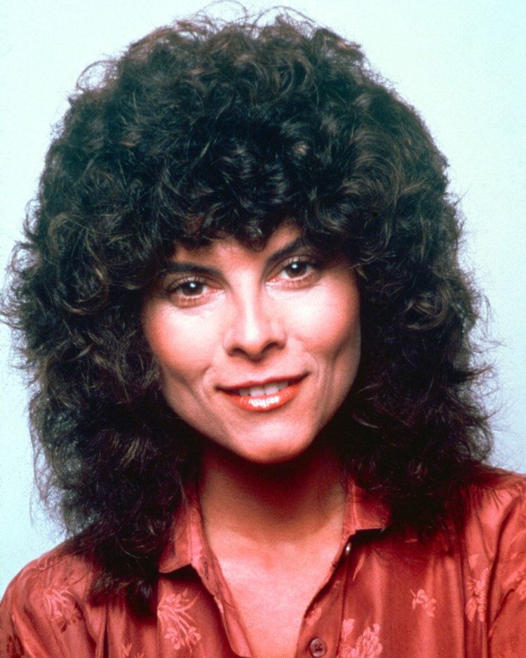 Adrienne Barbeau smiling, with curly hair, and wearing a red polo shirt.