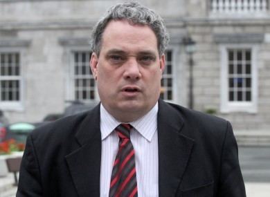 Aengus Ó Snodaigh wearing black coat, white long sleeves and black and red neck tie