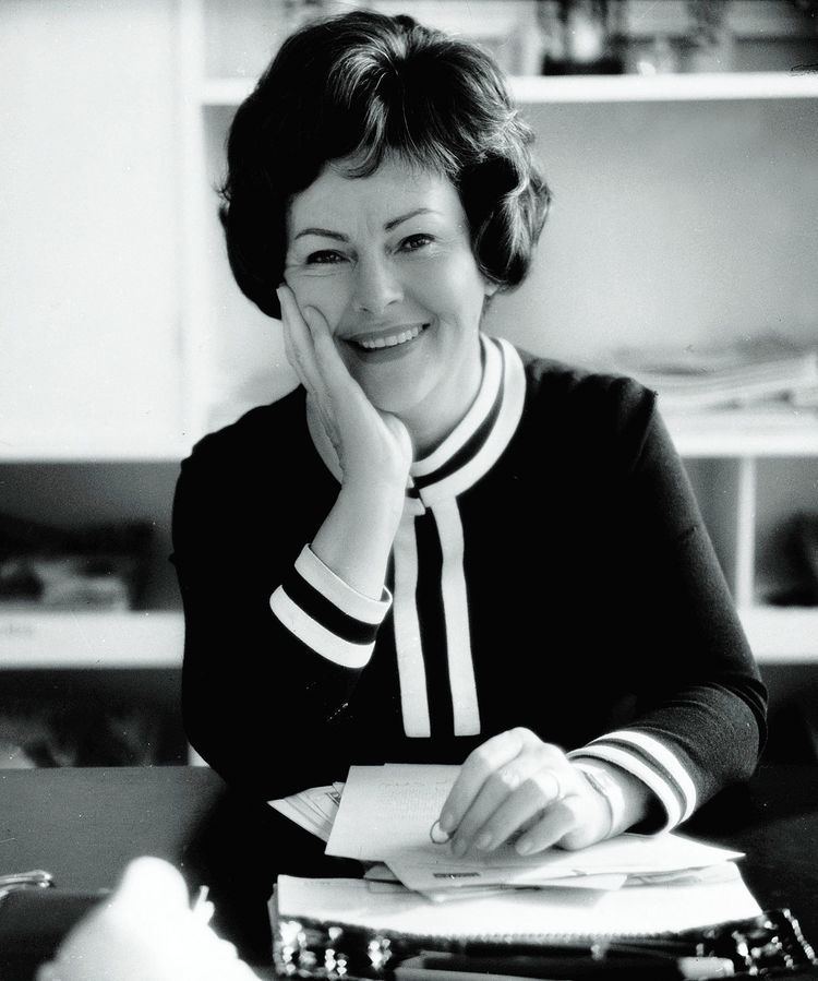 Aenne Burda smiling with his hand on her face and wearing a longsleeve black and white dress.