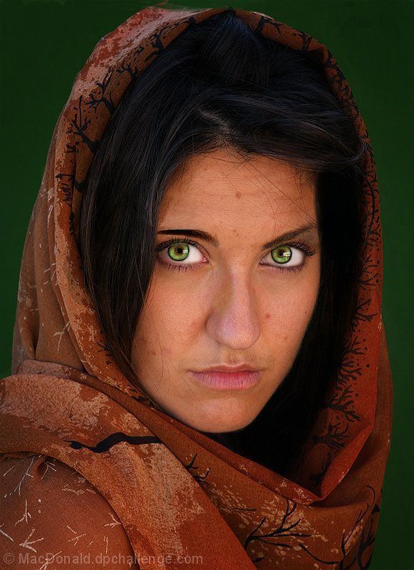 A woman with green eyes staring directly into the camera, and wearing a maroon scarf draped loosely over her head.