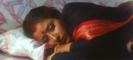 Manisha Koirala lying on the bed while wearing a black and red dress in a scene from the 1996 Indian Hindi drama film, Agni Sakshi