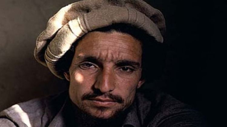 Ahmad Shah Massoud posing inside a building wearing a brown desert hat and light gray clothing.