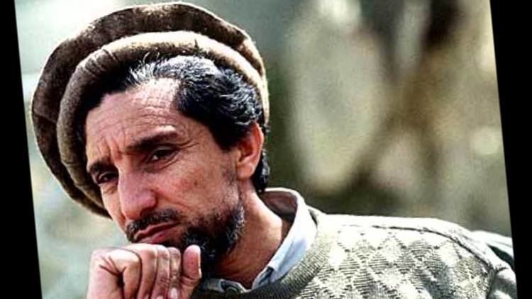 Ahmad Shah Massoud wearing a brown desert hat and checkered clothing with his hand on his chin.