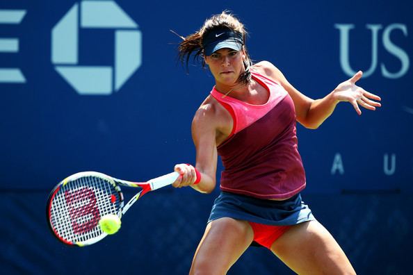 Ajla Tomljanovic playing tennis while wearing a pink top, blue skirt and blue cap