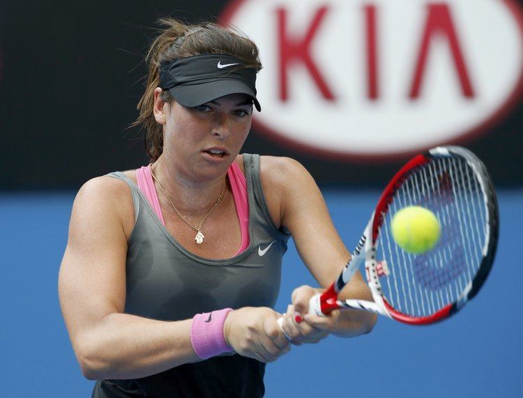 Ajla Tomljanovic playing tennis while wearing a black cap and gray top